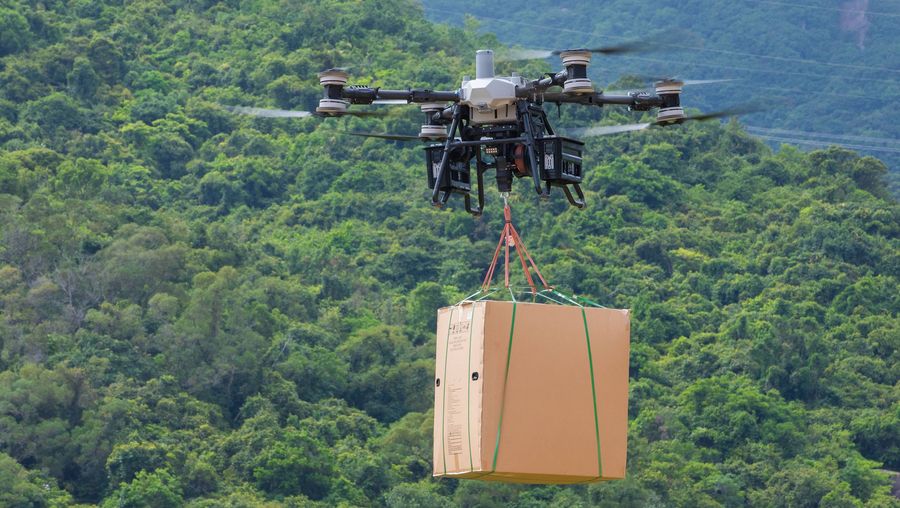 DJI heavy-lift delivery drone carrying a slung load over forest