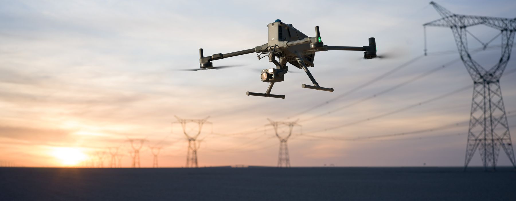 Inspection drone flying a transmission line corridor at sunset